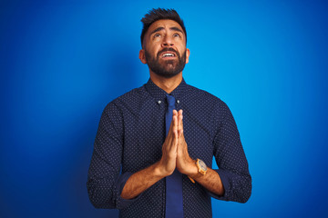 Young indian businessman wearing elegant shirt and tie standing over isolated blue background...