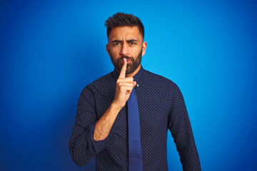Young indian businessman wearing elegant shirt and tie standing over isolated blue background...