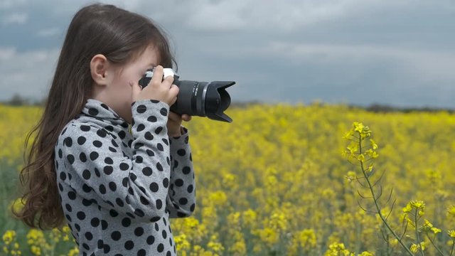 Young photographer. Cute little girl with a camera on a yellow flowering field.