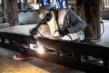 Industrial Worker at the factory welding closeup. Electric wheel grinding on steel structure in factory.