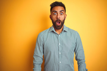 Obraz premium Young indian man wearing green striped shirt standing over isolated yellow background afraid and shocked with surprise expression, fear and excited face.