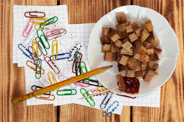 On the table in a mess of scattered multi-colored clips to attach notes, pieces of paper to study. Next is a plate of fried crackers and sauce for fast food during school.