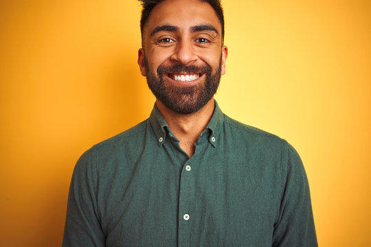 Young indian man wearing green shirt standing over isolated yellow background with a happy and cool smile on face. Lucky person.