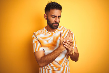 Young indian man wearing t-shirt standing over isolated yellow background Suffering pain on hands...