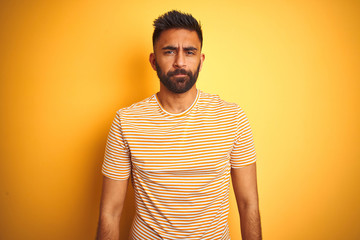 Obraz premium Young indian man wearing t-shirt standing over isolated yellow background depressed and worry for distress, crying angry and afraid. Sad expression.