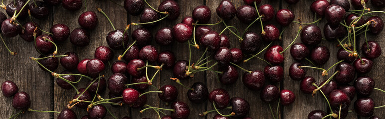 panoramic shot of fresh, sweet, red and ripe cherries covered with water drops on wooden table