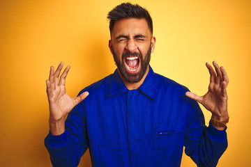 Handsome indian worker man wearing uniform over isolated yellow background celebrating mad and crazy for success with arms raised and closed eyes screaming excited. Winner concept