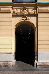 Yellow building in the sun with dark, shadowed entrance leading into the dark with small lights disappearing into the unknown