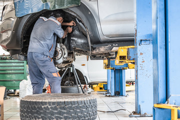 Car mechanic worker woking for reparing and replacing car's disk brake. Car without wheel and tire lifting at auto repair garage shop station.