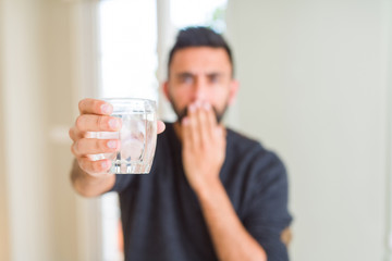 Handsome hispanic man drinking a fresh glass of water cover mouth with hand shocked with shame for mistake, expression of fear, scared in silence, secret concept