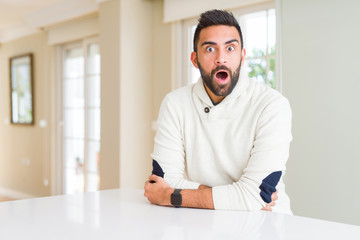 Naklejka premium Handsome hispanic man wearing casual white sweater at home afraid and shocked with surprise expression, fear and excited face.