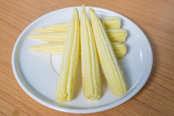 Young raw baby corn vegetables on white plate.