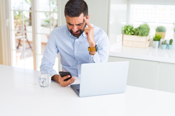 Handsome hispanic business man using laptop and smartphone serious face thinking about question,...