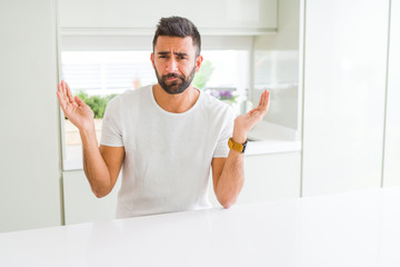 Handsome hispanic man casual white t-shirt at home clueless and confused expression with arms and...