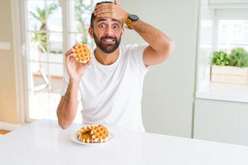 Handsome hispanic man eating sweet belgian waffle pastry stressed with hand on head, shocked with shame and surprise face, angry and frustrated. Fear and upset for mistake.