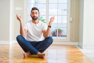 Handsome hispanic man wearing casual t-shirt sitting on the floor at home relax and smiling with eyes closed doing meditation gesture with fingers. Yoga concept.