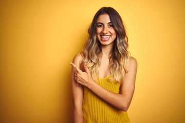 Obraz premium Young beautiful woman wearing t-shirt over yellow isolated background cheerful with a smile on face pointing with hand and finger up to the side with happy and natural expression