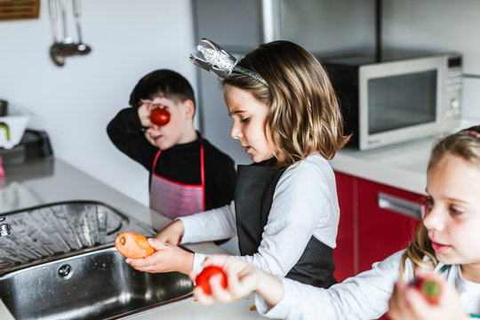 Little girls and boy cutting and peeling ripe vegetables while cooking healthy salad in kitchen together