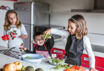 Little girls and boy Kids playing while while cooking healthy salad in kitchen together