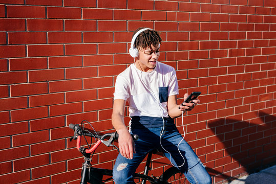 Young happy black male listening music with smartphone on bike