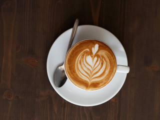 Overhead fresh brewed cappuccino coffee in white ceramic cup, saucer, spoon with beautiful handmade...
