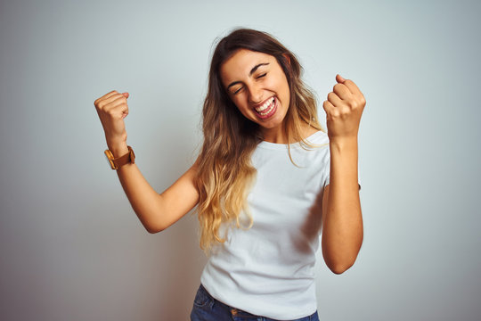 Young beautiful woman wearing casual white t-shirt over isolated background very happy and excited doing winner gesture with arms raised, smiling and screaming for success. Celebration concept.
