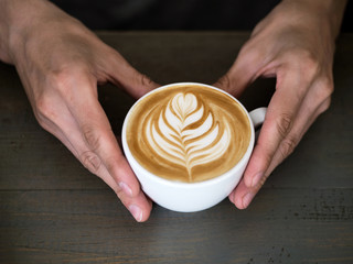 Male barista hands holding cup of fresh delicious cappuccino with latte art cream foam, brewed and made with love and take care concept, good service coffee shop