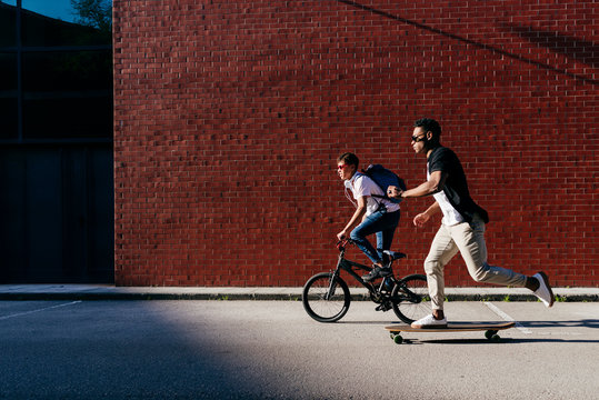 Young African American men riding bicycle and skateboard