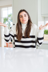 Beautiful young woman wearing stripes sweater clueless and confused expression with arms and hands...