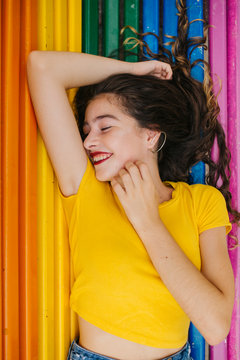 Pretty young female in casual outfit cheerfully closed eyes while lying on rainbow bench background