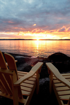 Two deck chairs facing a beautiful seaside sunset.