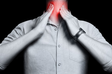 Man touching his neck, having a throat irritation, isolated on black background