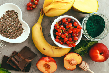Superfoods and healthy food on a gray background with copy space Fruits: mango, banana, currant, peaches lie next to chia and spirulina seeds Top view Copy space Selective focus