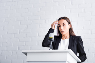 worried lecturer, suffering from glossophobia, holding napkin near forehead while standing on podium tribune