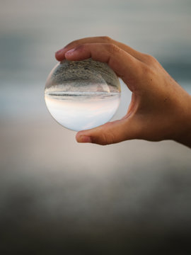 Crop View Of Little Female Child With Brown Hair Holding Glass Ball On Background Of Waves