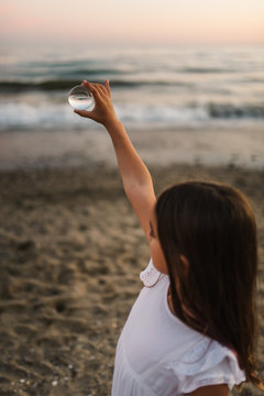 Side view of little female child with brown hair holding glass ball on background of waves