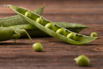 Open pea pods close-up. Green peas on wooden background.