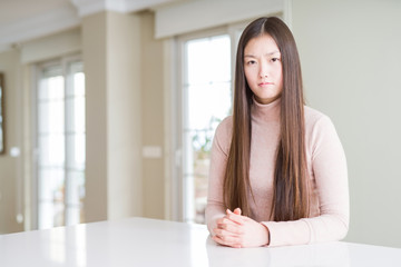 Beautiful Asian woman wearing casual sweater on white table skeptic and nervous, frowning upset...