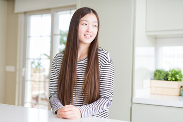 Beautiful Asian woman wearing stripes sweater looking away to side with smile on face, natural expression. Laughing confident.
