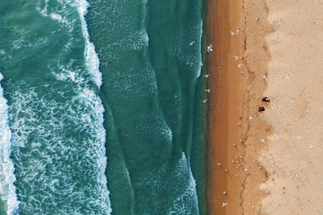 Scenic aerial view of golden sand waves and turquoise sea water with white foam from small waves. The concept of summer holidays. Bright abstract background perfect for any design