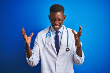 African american doctor man wearing stethoscope standing over isolated blue background celebrating mad and crazy for success with arms raised and closed eyes screaming excited. Winner concept