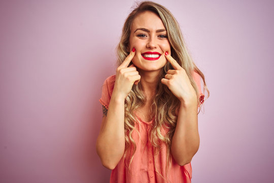 Young beautiful woman wearing t-shirt standing over pink isolated background Smiling with open mouth, fingers pointing and forcing cheerful smile