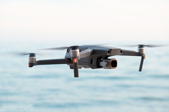 Professional filming drone flies in the air at a low altitude against a blue sky and sea sandy beach. Drone makes photos. Modern new technology. Ready background with place for your text.