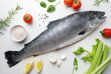 Fresh salmon fish lies on a white table. Ingredients for cooking fish, rosemary, basil, cherry tomatoes, spinach leaves, celery, lemon, garlic, spices, Hawaiian salt. Sea fish with red meat. Omega B3