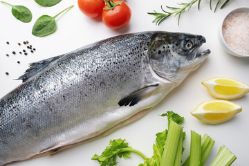 Fresh salmon fish lies on a white table. Ingredients for cooking fish, rosemary, basil, cherry tomatoes, spinach leaves, celery, lemon, garlic, spices, Hawaiian salt. Sea fish with red meat. Omega B3