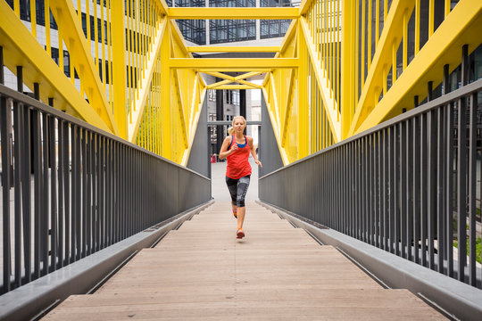 European Quarter, Stuttgart, Baden-W&cedil;rttemberg, Germany: A female runner running up stairs covered in a fancy, yellow steal construction.          