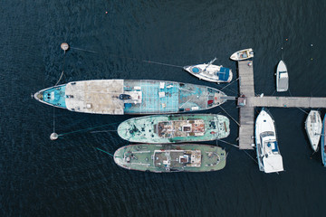 Aerial view of the old pier with old rusty yachts, boats and fishing boats moored against a background of blue water. Texture of water with small waves. Copyspace