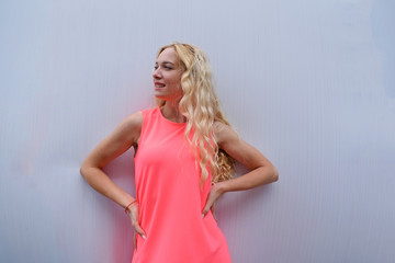 Beautiful blonde girl in pink dress on white wall background.