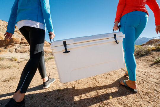 Two women carry a cooler while camping during a windy spring day at the Alabama Hills near Lone Pine, California.