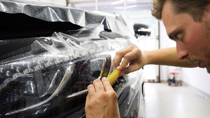 Close up to PPF installation process on a front headlight and hood. PPF is a Paint Protection Film which protect paint from scratches and stone chips. Concept of: Guard, Protect, Car, New, Work.